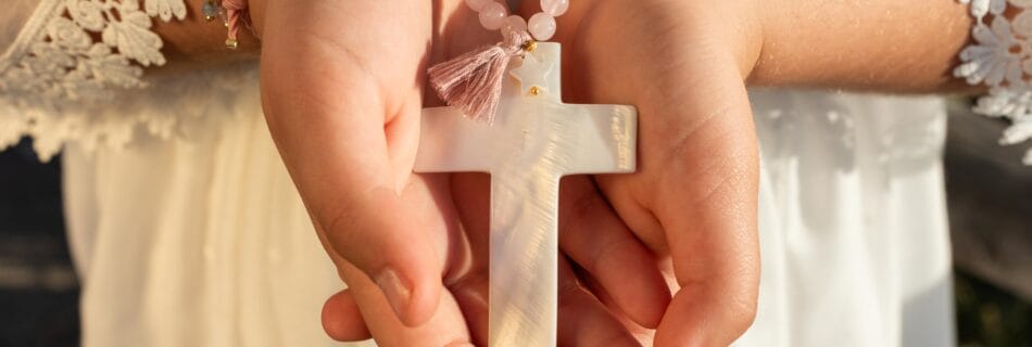 Primer plano de las manos de una niña sosteniendo un rosario con una cruz, vestida de comunión cruz entre las manos de una niña