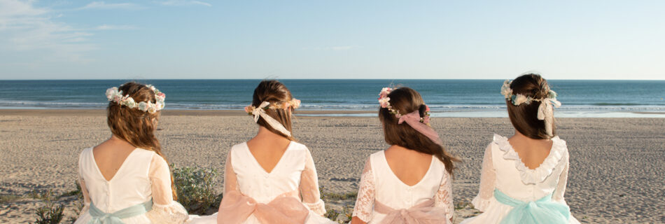 Cuatro niñas con vestidos de comunión sentadas de espaldas en la playa mirando el mar de Cádiz