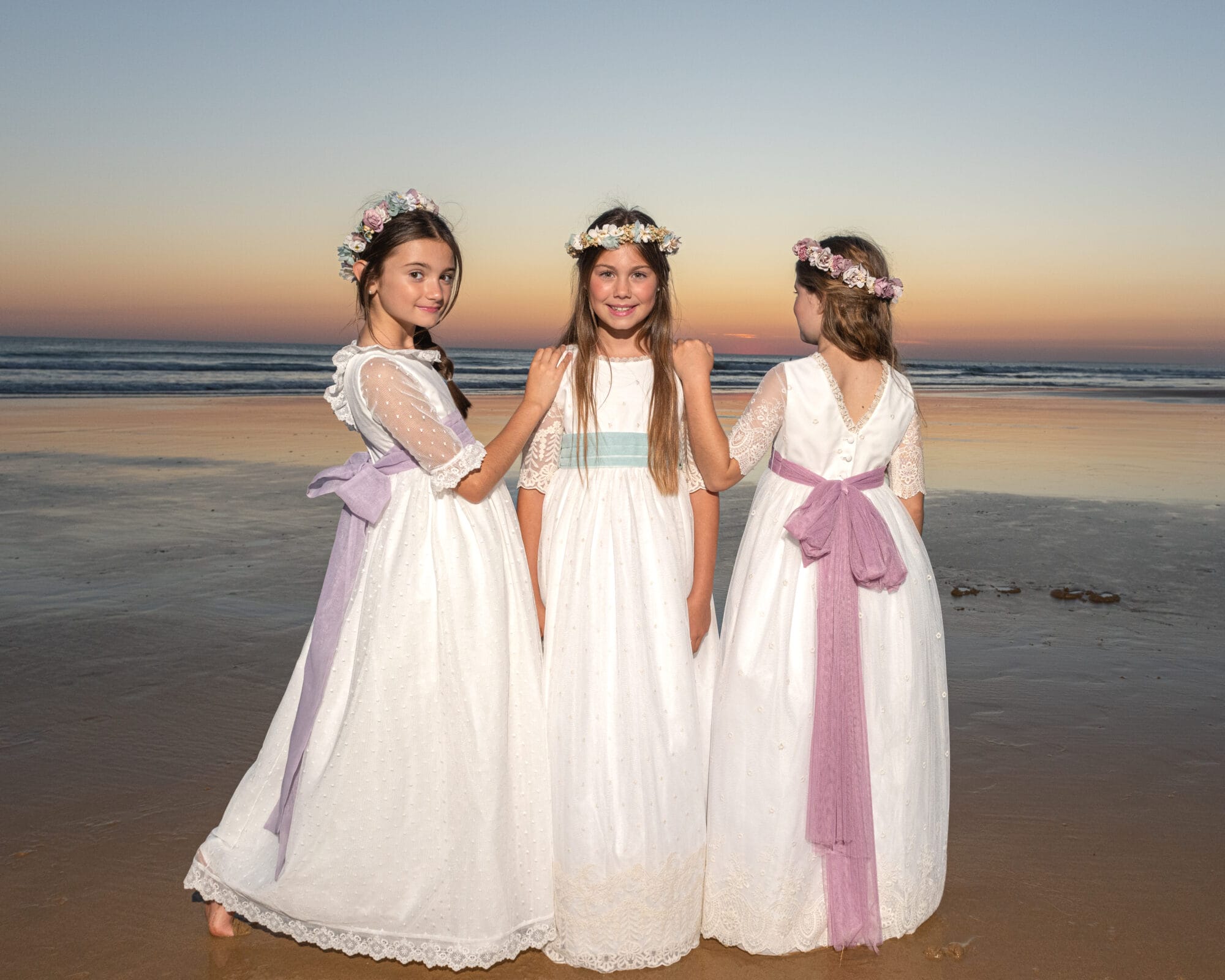 Tres niñas con vestidos de comunión posando en la playa al atardecer en Cádiz
