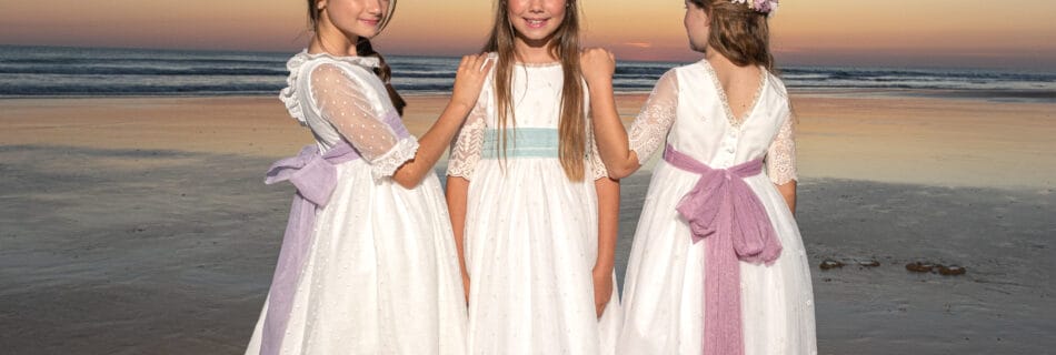Tres niñas con vestidos de comunión posando en la playa al atardecer en Cádiz