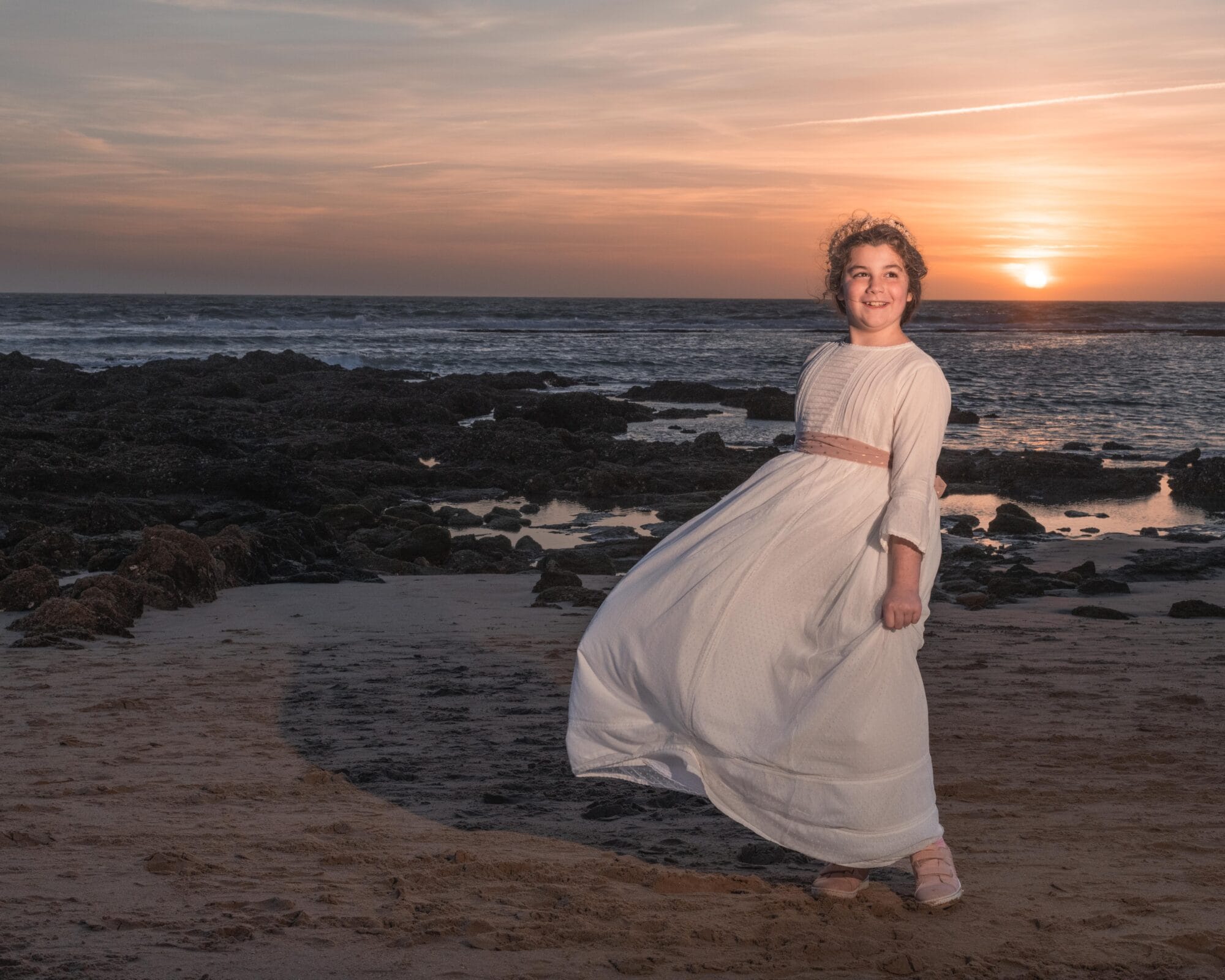 Niña con vestido de comunión blanca posando en la playa al atardecer en Málaga
