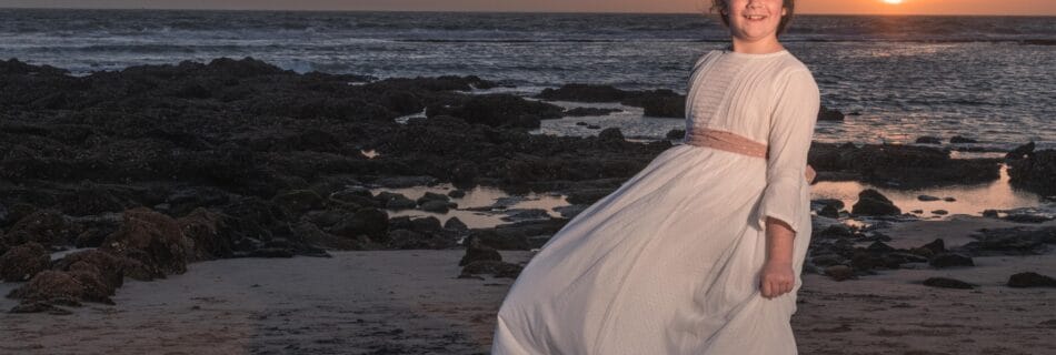 Niña con vestido de comunión blanca posando en la playa al atardecer en Málaga