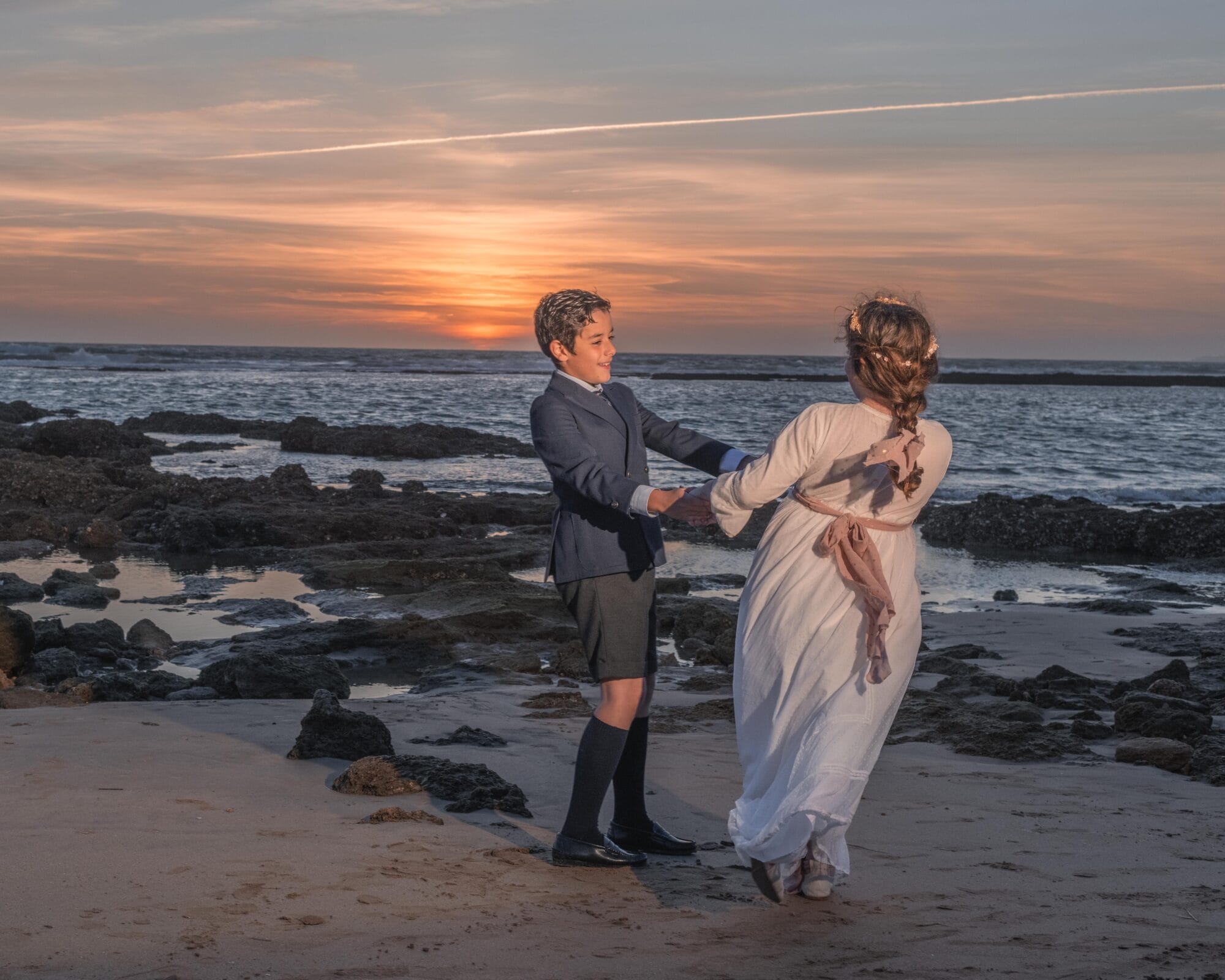 Niños vestidos de comunión jugando en la playa al atardecer en el Puerto de Santa María