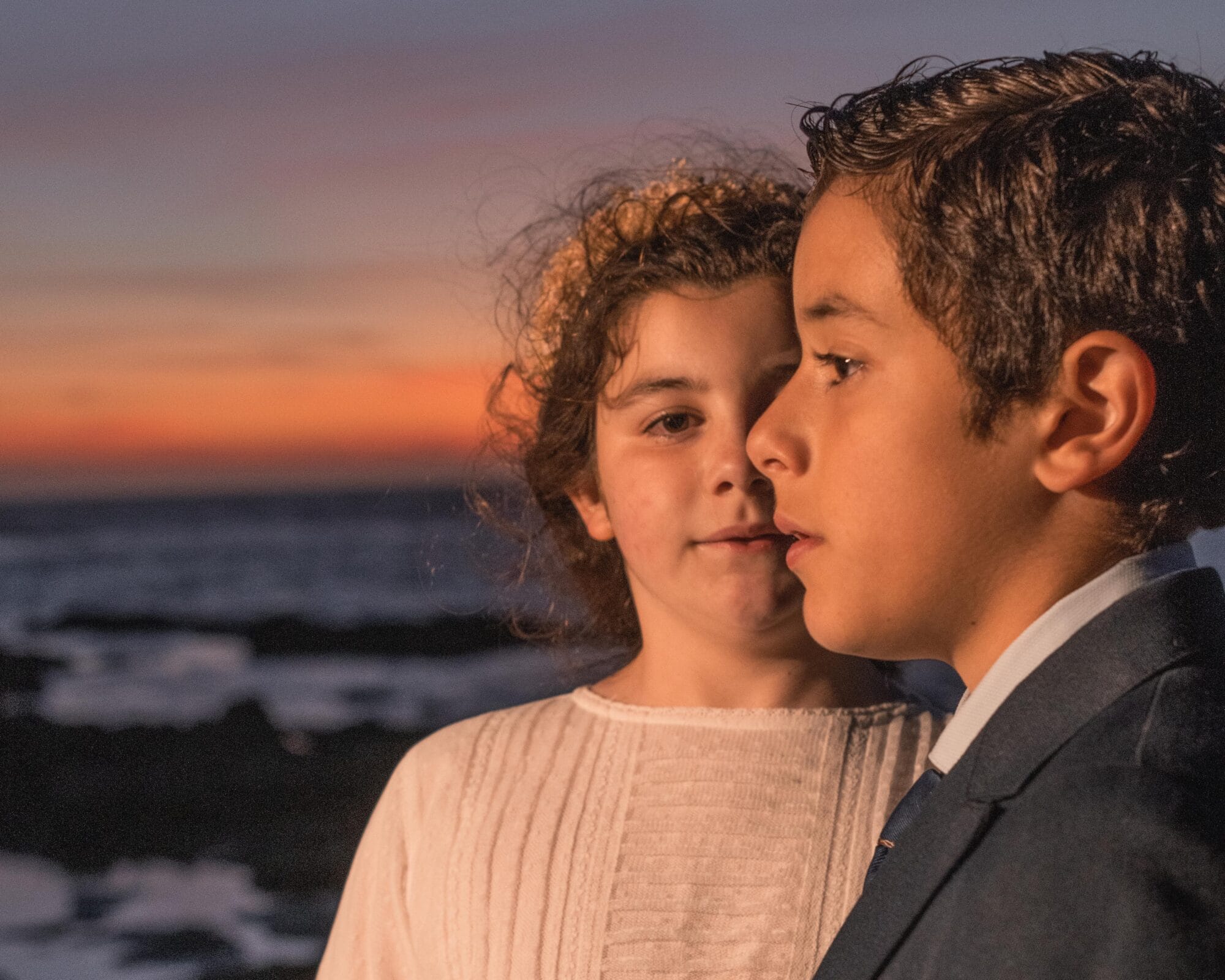 Dos niños mellizos vestidos para una comunión al atardecer en la playa de Cádiz