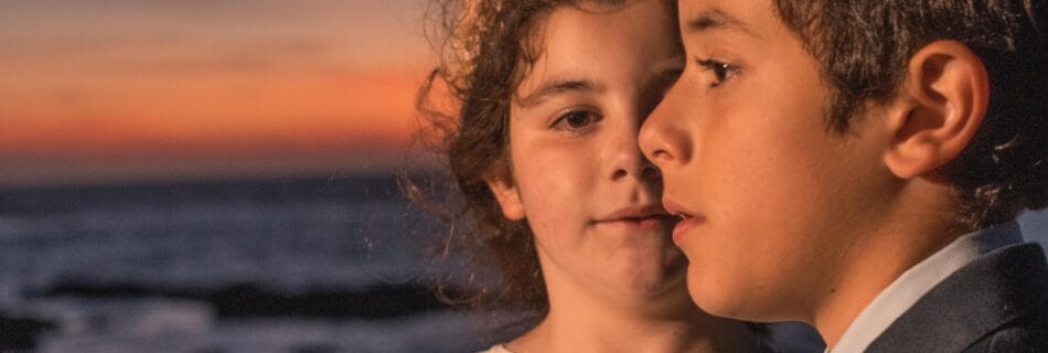 Dos niños mellizos vestidos para una comunión al atardecer en la playa de Cádiz