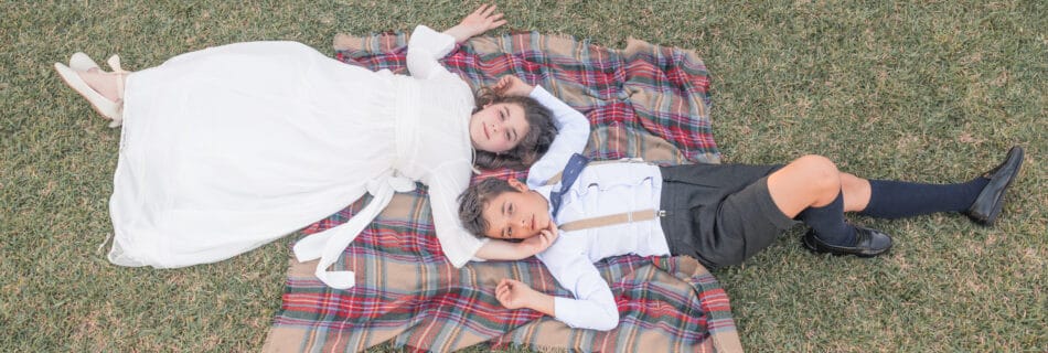 Niña con vestido de comunión y niño con tirantes acostados en una manta en el césped en Jerez