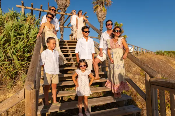 Foto familiar en la arena con padres e hijos abrazados, luz cálida y ambiente alegre.