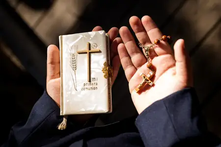 Detalle de manos sujetando Biblia y cruz de comunión